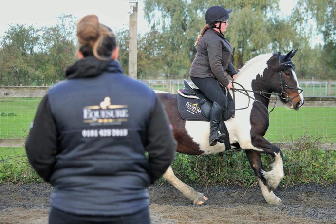 Teacher wearing Equesure clothing teaching a rider going around a paddock