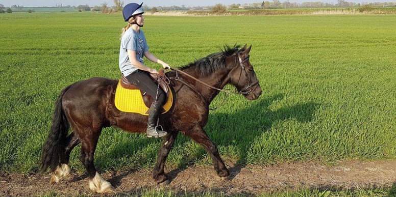 Christie riding Travis through a field