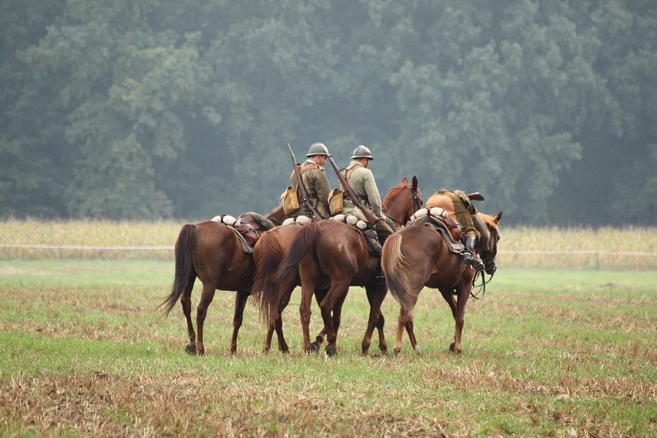 Three horses carrying soldiers walking across a field