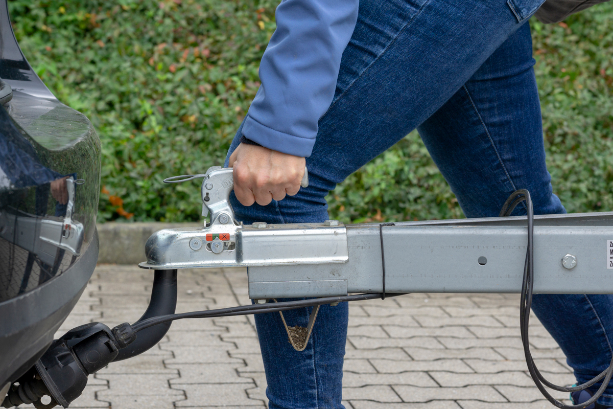 A person attaching a trailer to the towbar of a car