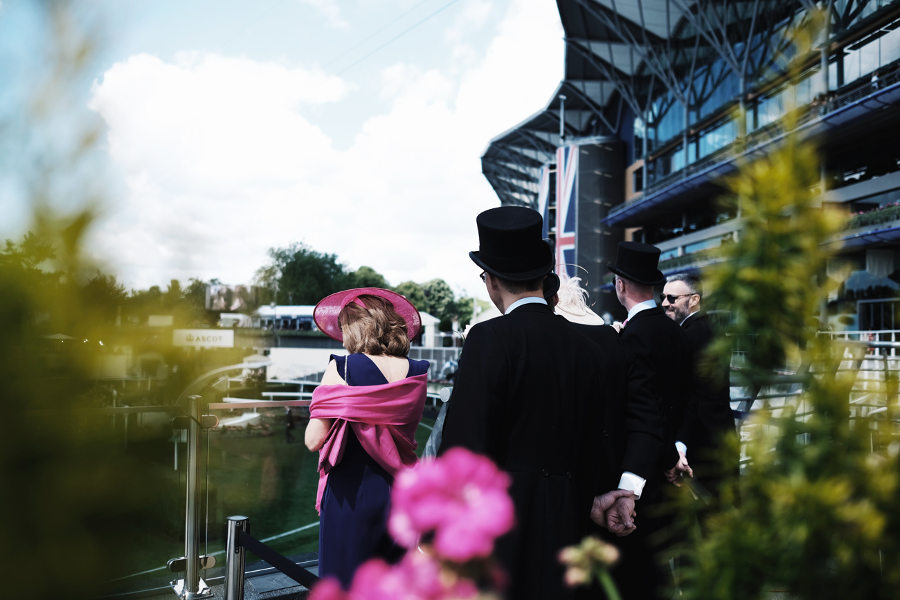 Smartly dressed people standing on a balcony at Ascot watching the races